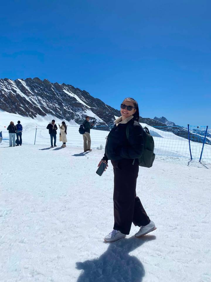 Woman standing on a snowy plateau with other tourists and a mountain ridge behind.