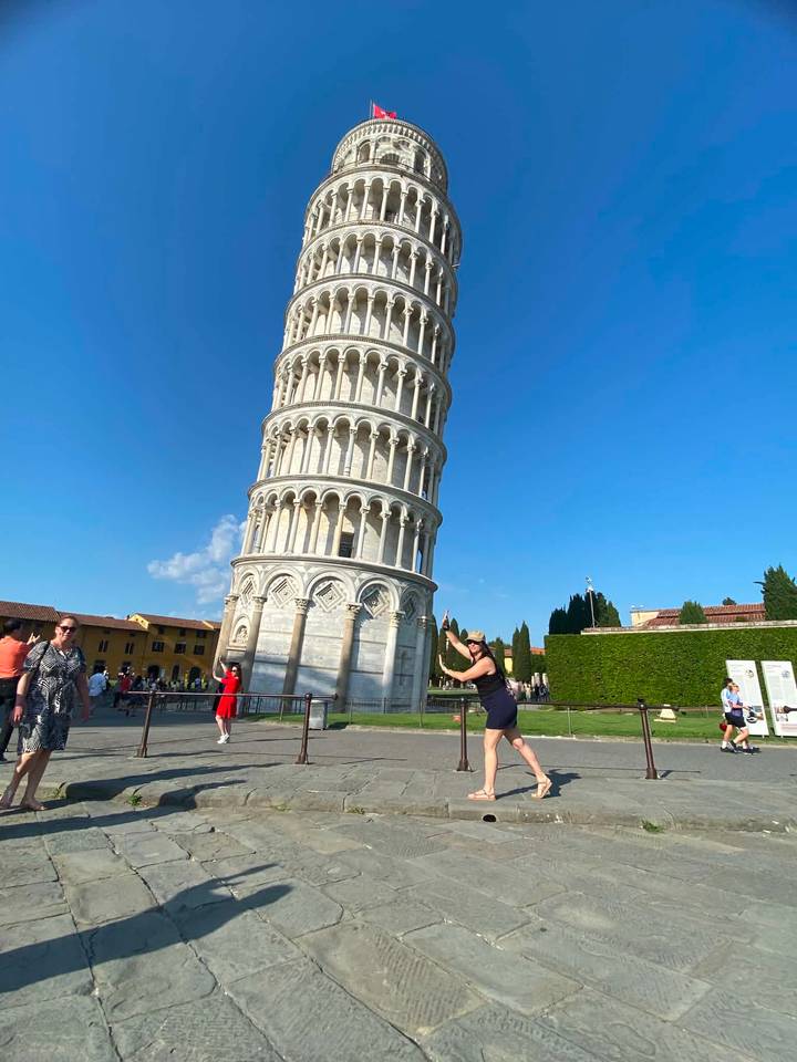 Tourists playfully posing to hold up the Leaning Tower of Pisa on a sunny day.