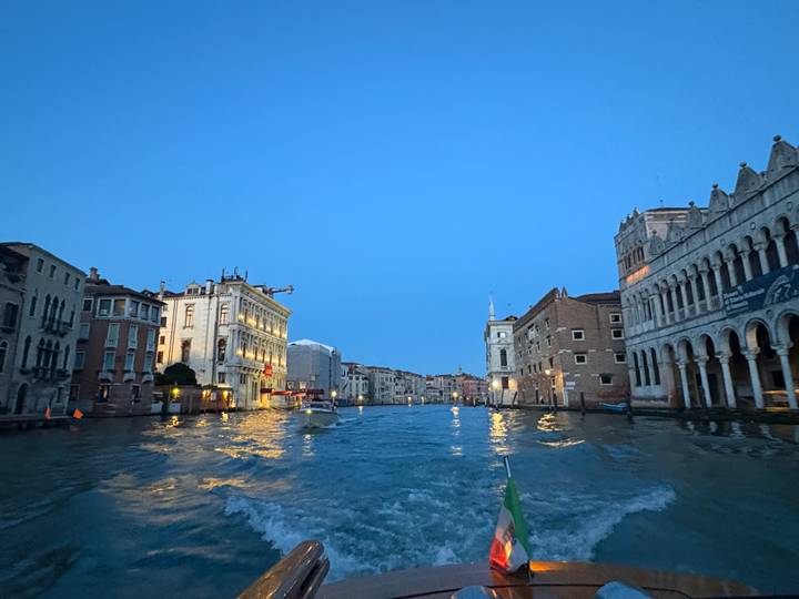 Dusk view from a canal boat gliding through Venice’s Grand Canal with historic buildings lit up.