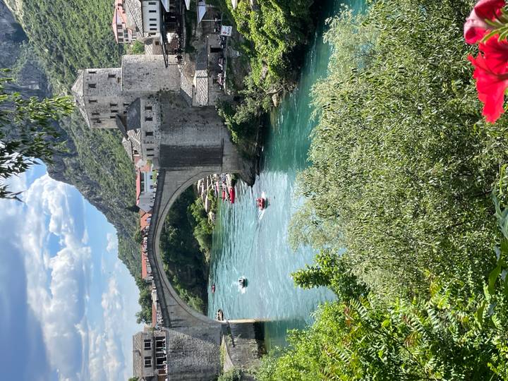 Famous Stari Most stone arch bridge spans emerald Neretva River amid mountains.