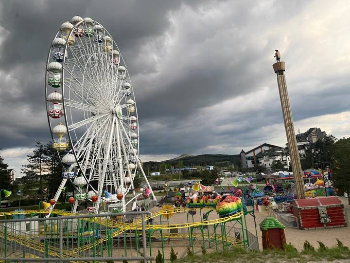 Amusement park with giant ferris wheel, colourful rides and dark storm clouds above.