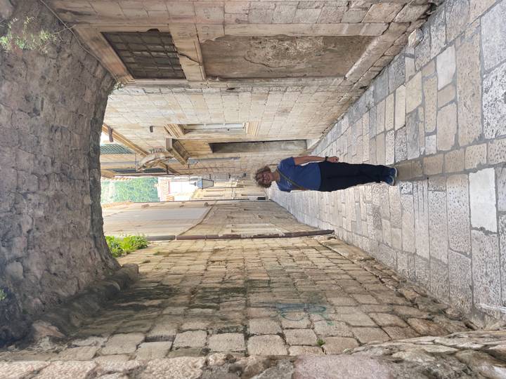 Traveller poses under narrow stone archway in a quiet medieval alley.