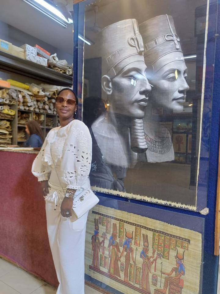 Traveller in white outfit poses before Egyptian papyrus art in a workshop.