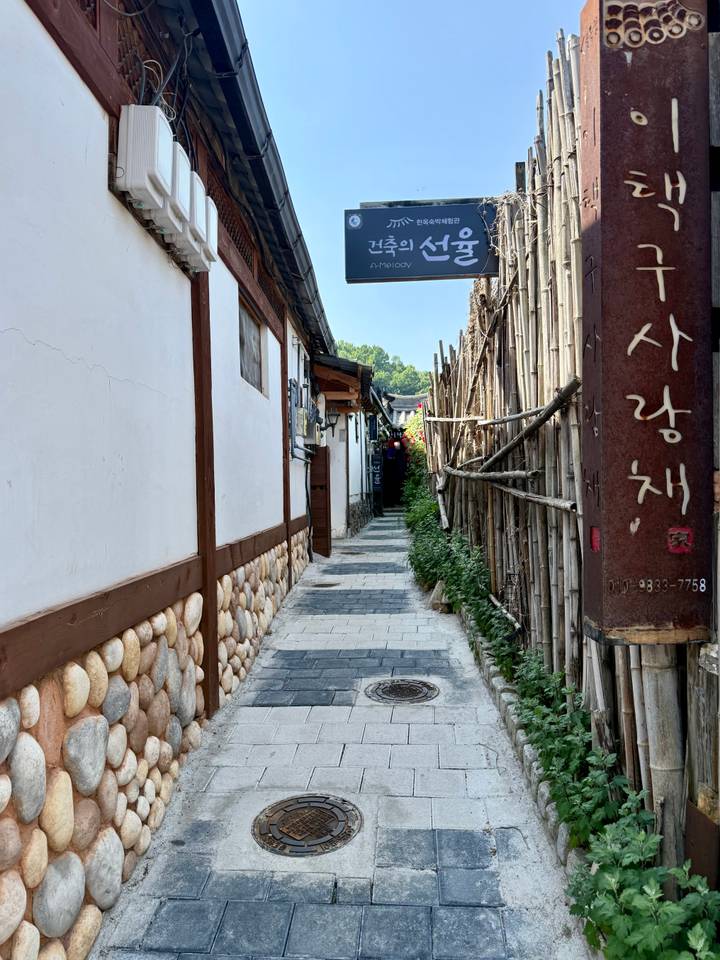 Narrow lane lined with stone walls and bamboo fences in a hanok village.