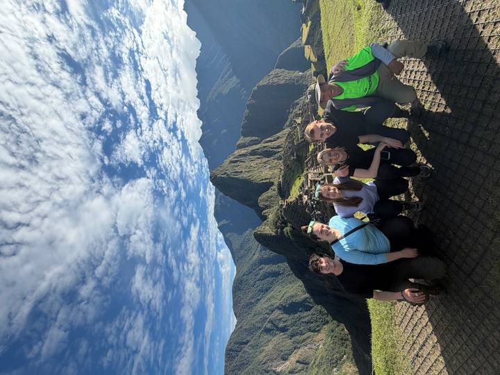Group of hikers kneel together with Machu Picchu ruins and Huayna Picchu behind.