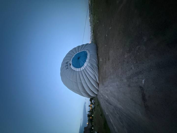 Deflated hot air balloon envelope lying on an open field in early dawn light.
