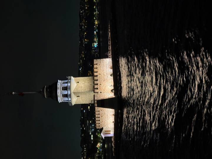 Istanbul’s Maiden’s Tower illuminated at night reflecting off dark Bosphorus waters.