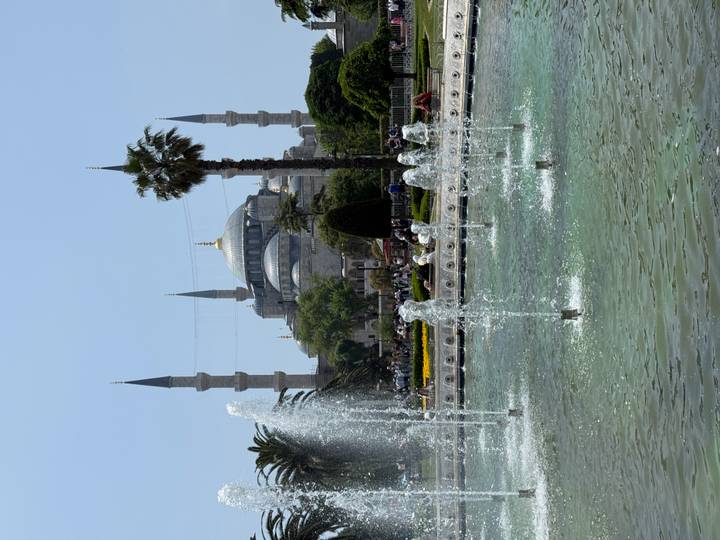 Blue Mosque rising beyond dancing fountains and palms on a sunny Istanbul afternoon.