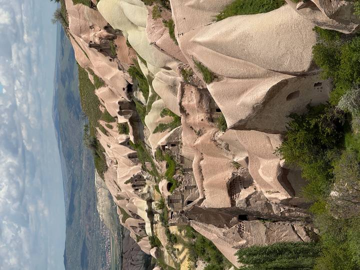 Sweeping view of Cappadocia’s pink-hued cave houses and eroded rock formations across rolling hills.