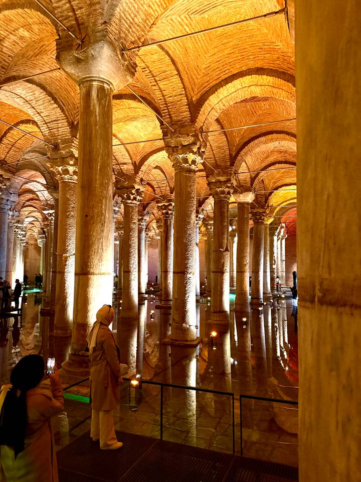 Illuminated rows of ancient stone columns reflecting in shallow water inside a historic underground cistern.