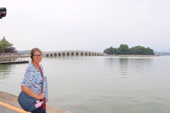 Woman posing beside Kunming Lake with the 17-Arch Bridge of the Summer Palace in the distance