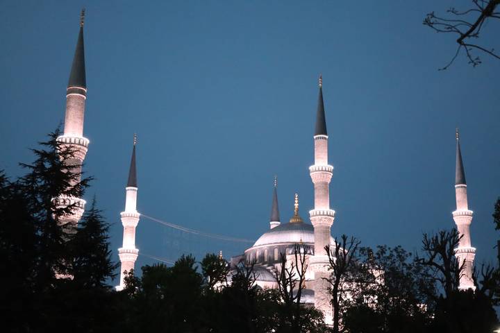 Illuminated minarets and domes of the Blue Mosque glowing against a deep twilight sky.