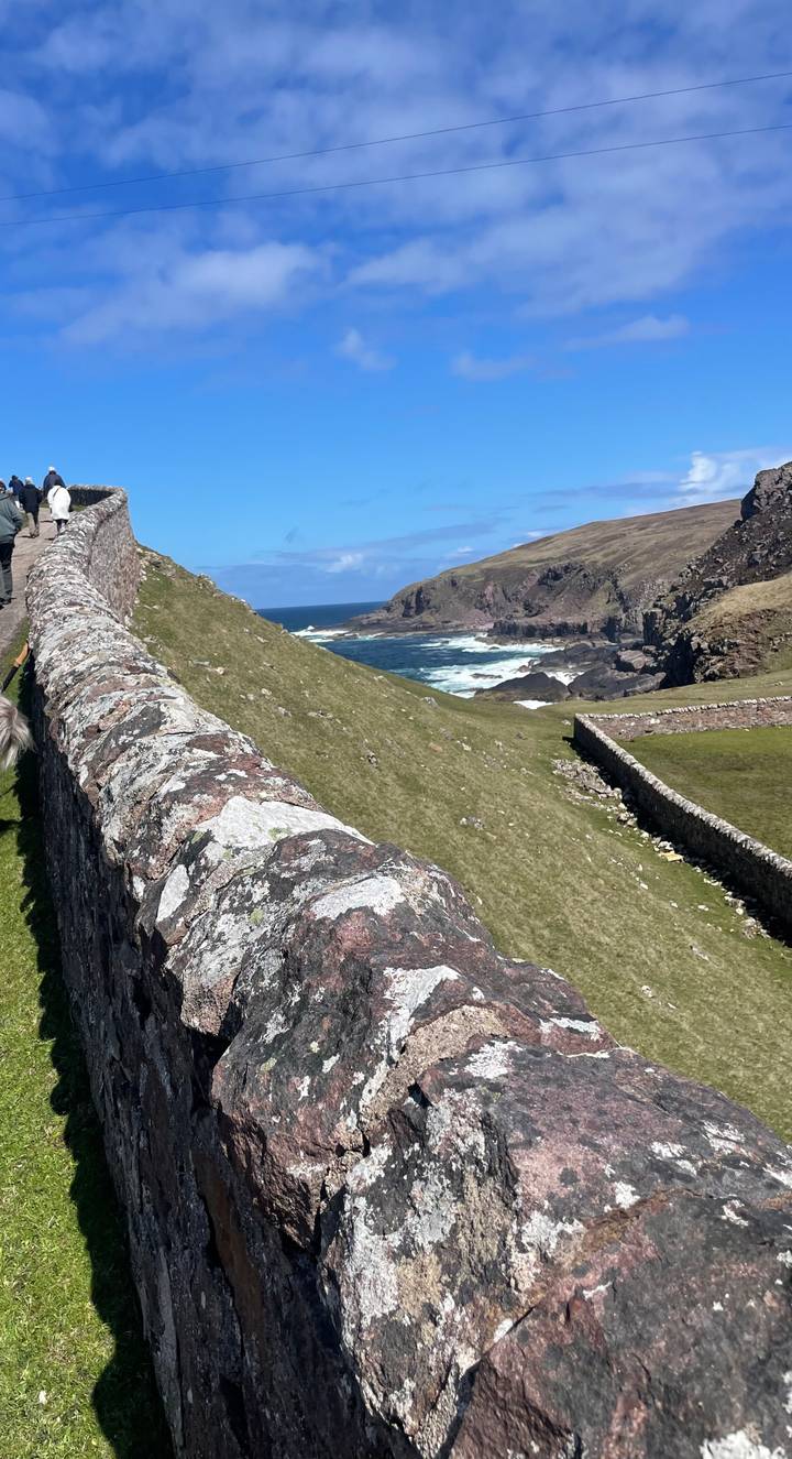 Stone coastal ruins overlooking rugged cliffs and crashing waves in northern Scotland.
