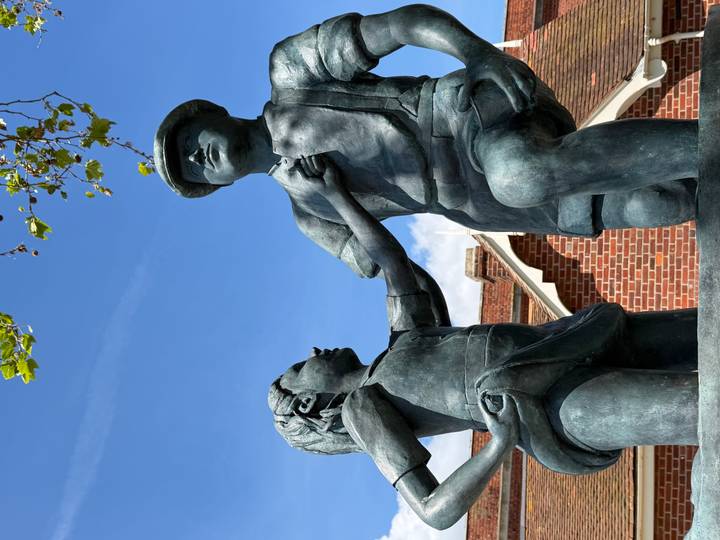 Bronze statue of two children outside a red-brick building under blue sky.