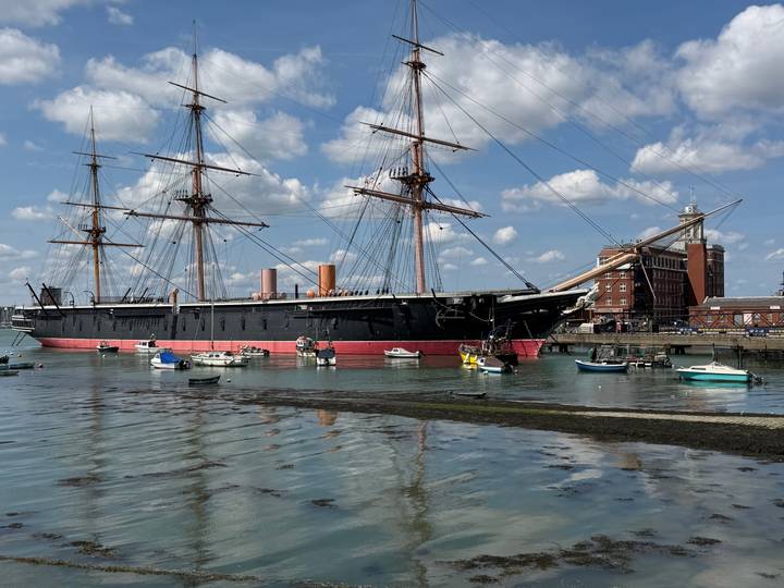 Historic ironclad warship HMS Warrior moored in a harbour with small boats and reflections.