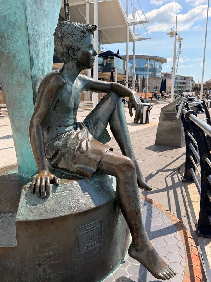 Bronze sculpture of a seated figure on a plinth in a modern plaza.
