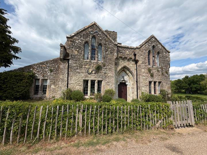 Historic stone building with Gothic windows and arched doorway in rural setting.