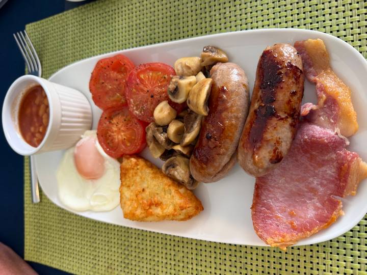 Traditional English breakfast plate with sausages, eggs, bacon, beans, tomatoes and mushrooms.