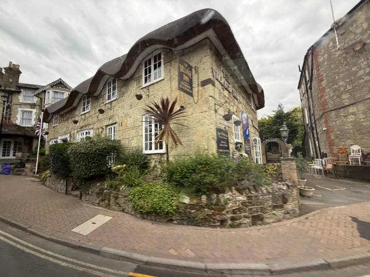 Motion-blurred street view of a rustic cottage with wavy roof captured from a moving vehicle.