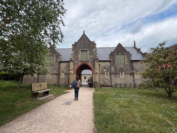Visitor walking toward a stone abbey entrance with arched gateway and grassy courtyard.