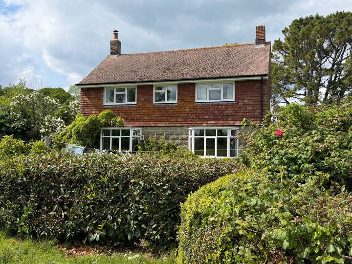 Two-storey country house surrounded by lush hedges and flowering shrubs.