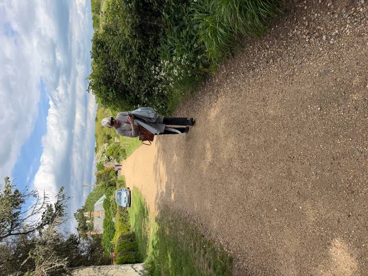 Woman walking down a gravel country path with hedgerows and distant cottages.