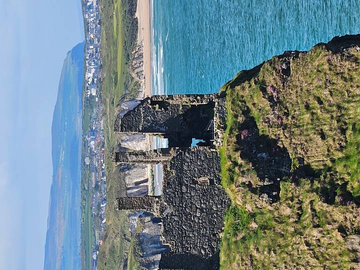 Clifftop ruins of Dunluce Castle overlooking turquoise sea and distant Causeway Coast.