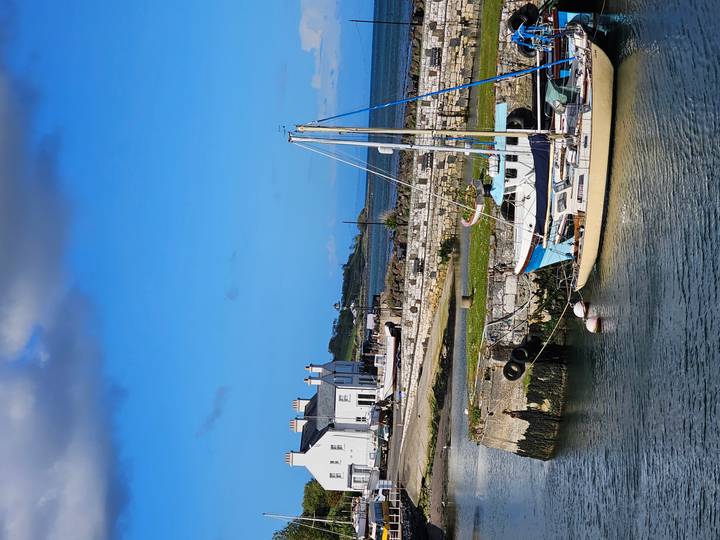 Small harbor with sailboat moored beside stone quay under bright blue Irish sky.