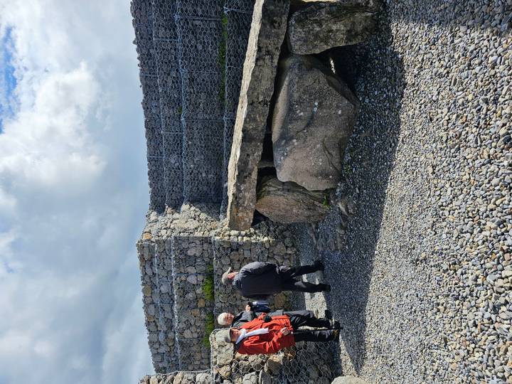 Visitors examining an ancient dolmen stone monument at an outdoor heritage site.