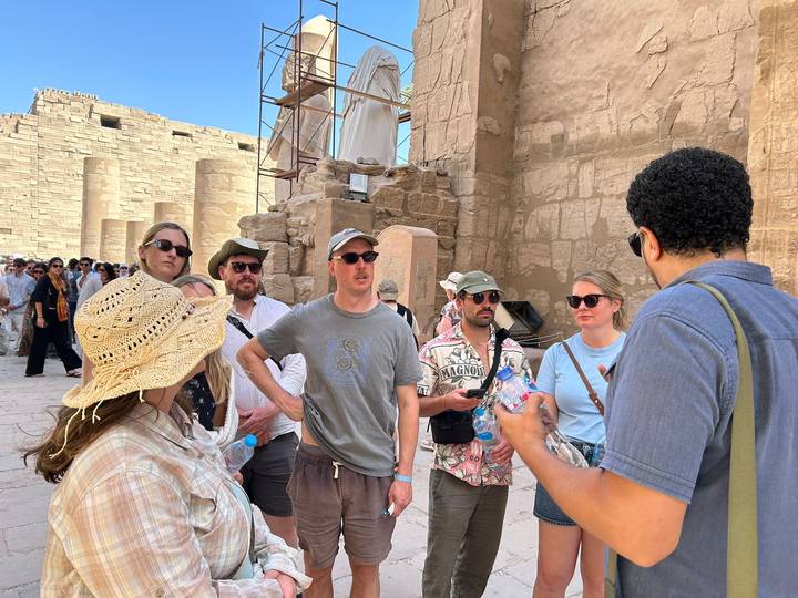 Tour guide explaining ancient ruins to attentive group inside Karnak Temple complex.