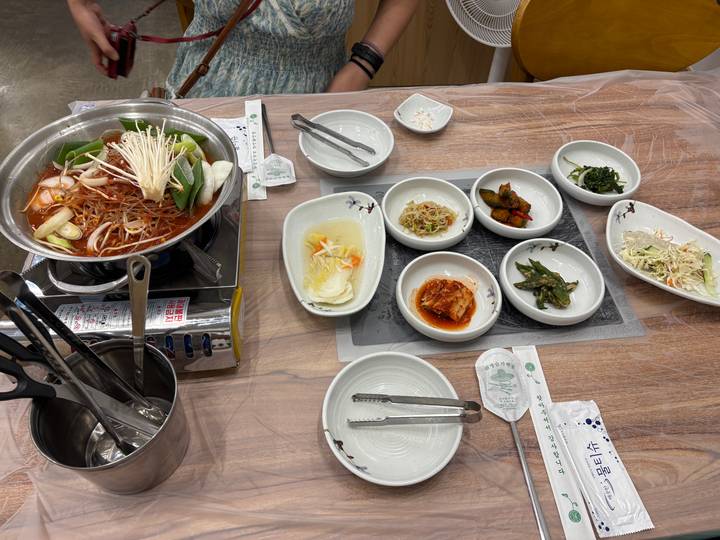 Traditional Korean meal setup with hotpot, kimchi and assorted banchan viewed from above on a wooden table.