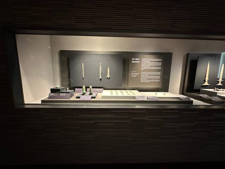 Glass museum case displaying ancient bronze daggers and small green artifacts with explanation panels.