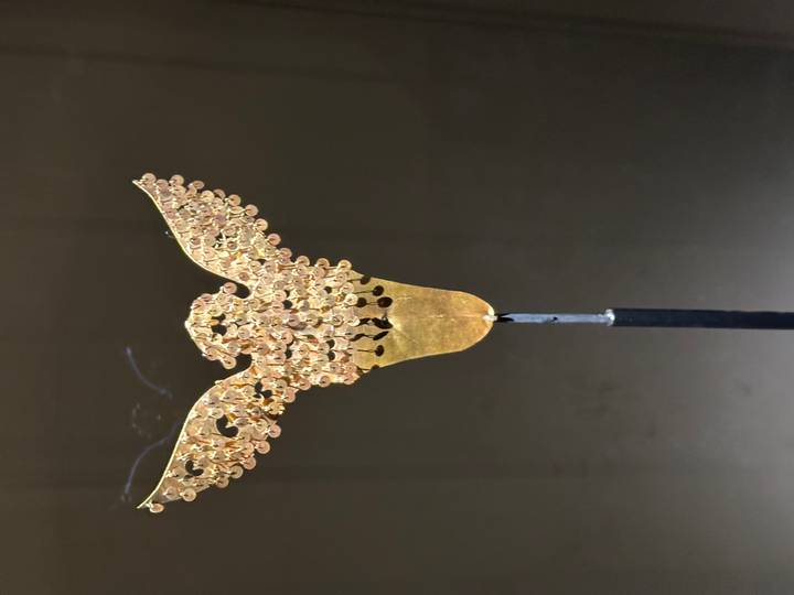 Close-up of a delicate gold phoenix-shaped ornament on a thin stand in a dark museum display.