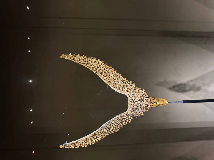 Gold crescent-shaped royal ornament with dangling beads displayed upright against a dark background.
