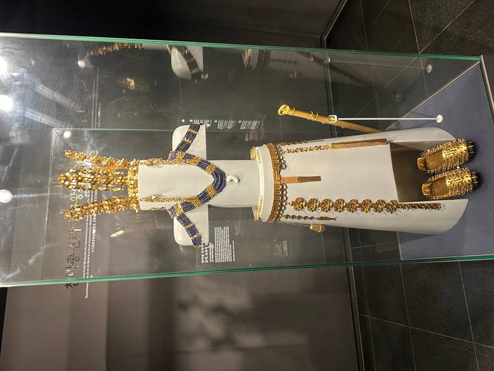 Full ceremonial gold regalia reconstructed on a white mannequin inside a glass museum case.