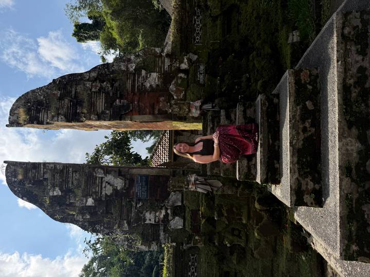 Traveler sitting on mossy stone steps between split Balinese temple gates.