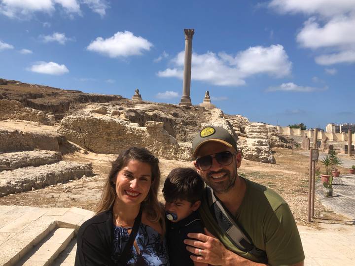 Smiling couple with sleepy child in front of ancient ruins and Pompey’s Pillar
