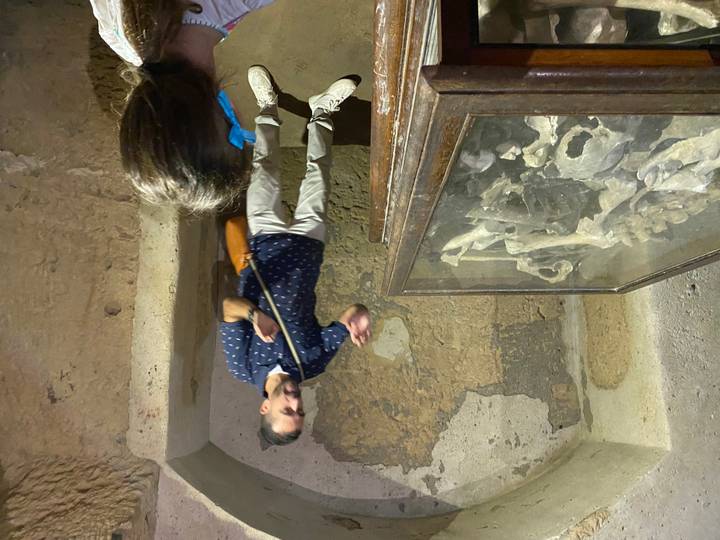 Guide explaining skeletal remains inside a dim archaeological catacomb chamber