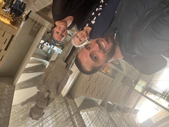 Three smiling travellers take a selfie with the Ramses II statue towering behind them inside the museum hall.