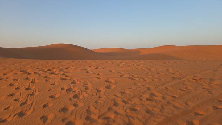 Undulating red-gold dunes stretch into the horizon under a clear evening sky.