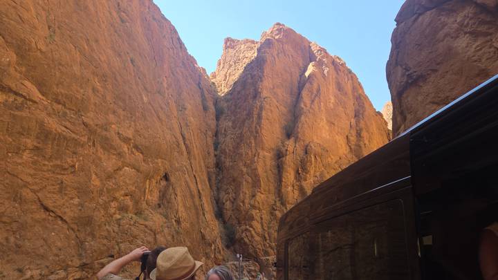 Steep orange canyon walls tower above visitors photographing the dramatic gorge.