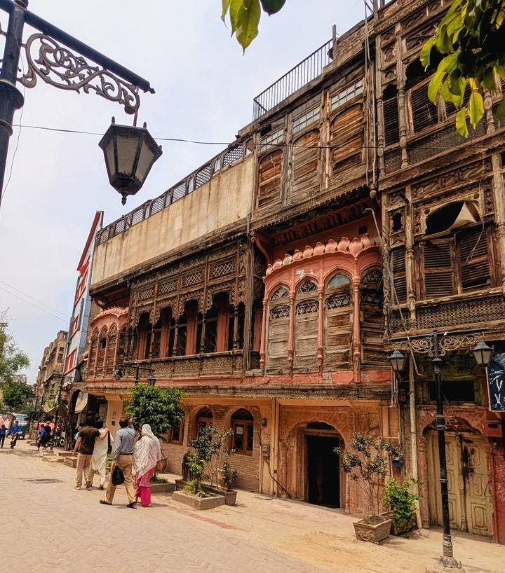 A weathered wooden merchant house with ornate balconies and carvings lines a historic street.