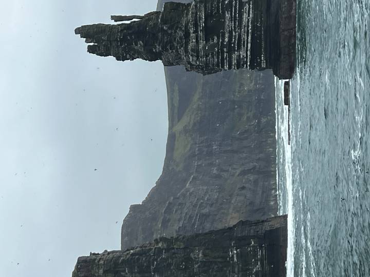 Dramatic sea cliffs rise vertically from rough Atlantic waters under a grey sky