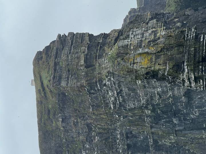Tower-topped sea cliff with layers of grey rock and lichen seen on an overcast day