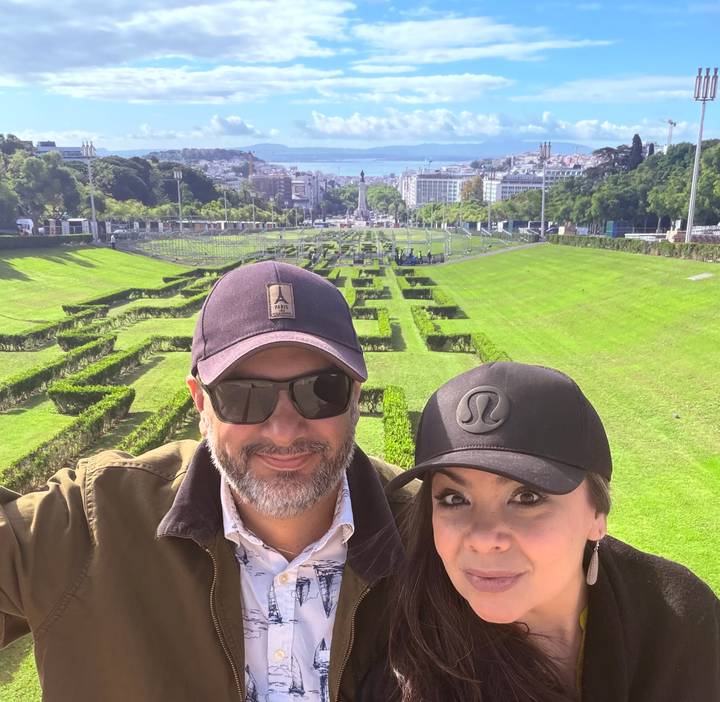 Couple taking a selfie with manicured hedges and a distant cityscape in the background