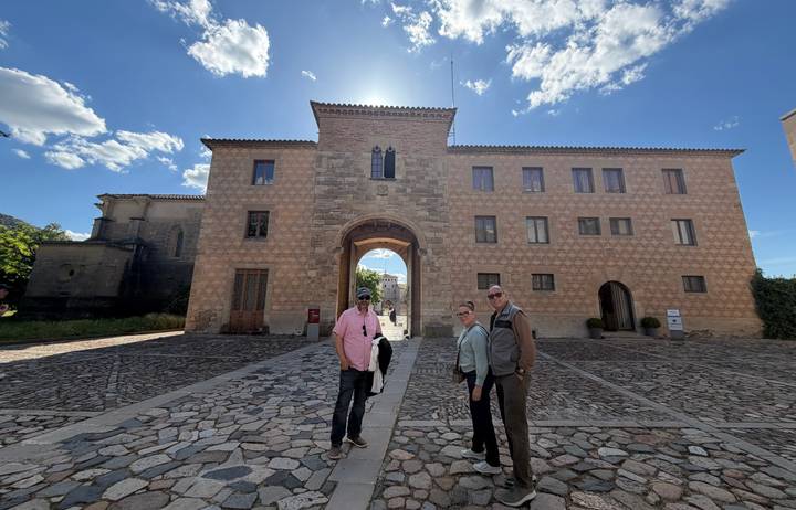 Three travelers standing in front of a historic stone complex with archway under bright sun