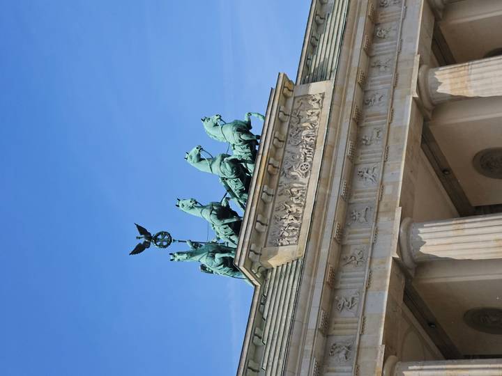 Close view of the Quadriga statues atop Brandenburg Gate against blue sky.