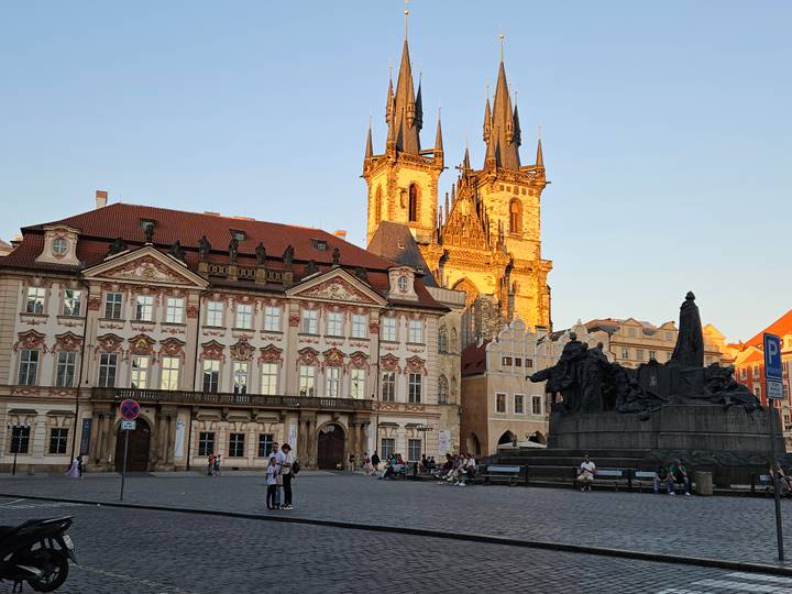 Prague Old Town Square with Týn Church illuminated at dusk and crowds below.