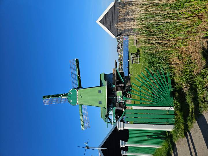 Traditional green windmill beside water and blue sky at Zaanse Schans.