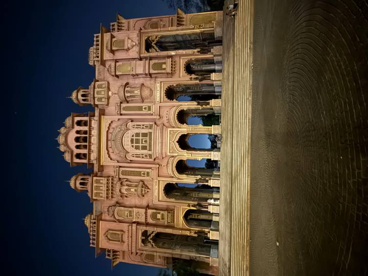 Night view of the illuminated pink Patrika Gate palace facade with deep blue sky above.